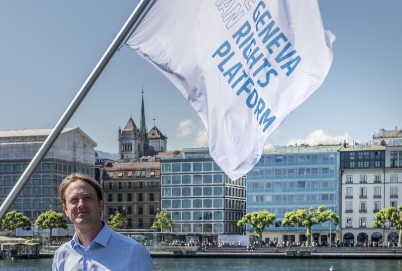 Felix Kirchmeier, Director of the plaform, in front of the flags of the Geneva Human Rights Platform on the Mont-Blanc Bridge